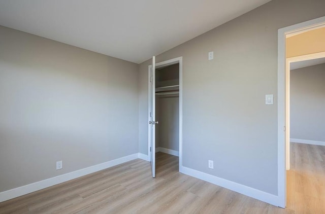 unfurnished bedroom with lofted ceiling, light hardwood / wood-style floors, and a closet