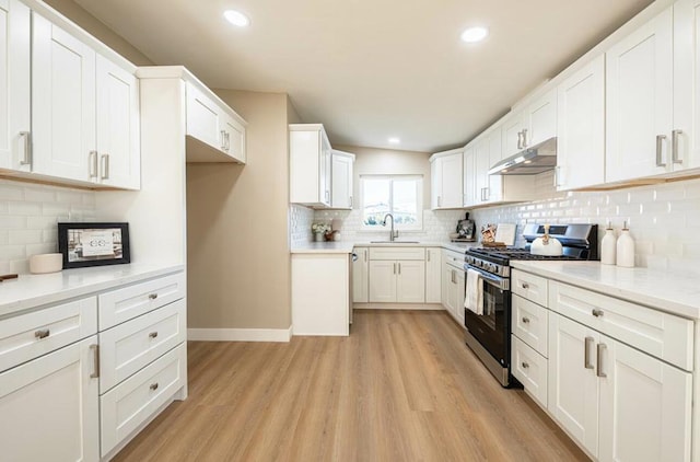 kitchen featuring stainless steel range with gas cooktop, sink, white cabinets, decorative backsplash, and light hardwood / wood-style floors