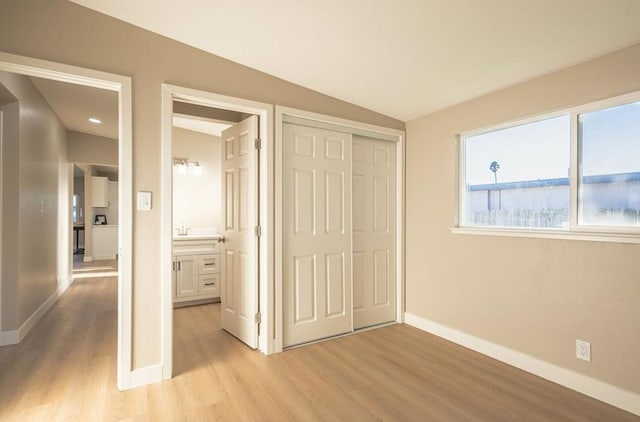 unfurnished bedroom featuring lofted ceiling, light hardwood / wood-style floors, and a closet