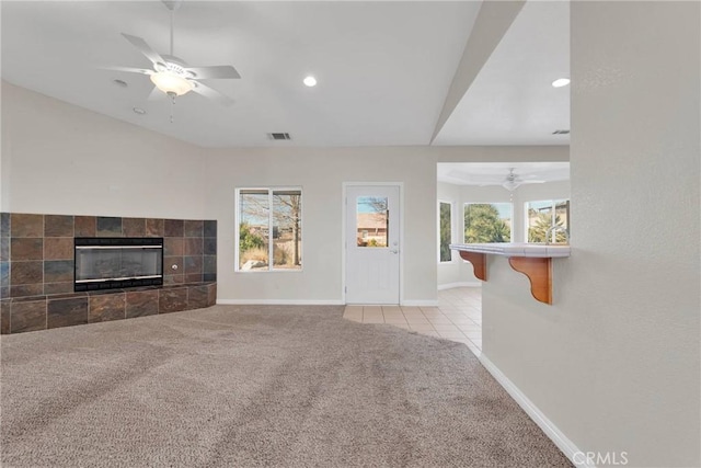 unfurnished living room featuring ceiling fan, light colored carpet, a tile fireplace, and vaulted ceiling