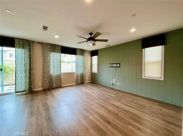 spare room with light hardwood / wood-style floors, wood walls, and ceiling fan