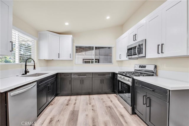 kitchen with lofted ceiling, sink, white cabinetry, light hardwood / wood-style flooring, and appliances with stainless steel finishes