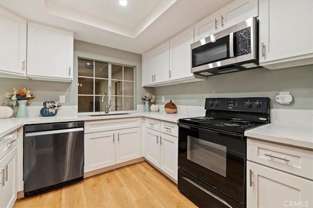 kitchen with sink, a tray ceiling, white cabinetry, light hardwood / wood-style flooring, and appliances with stainless steel finishes