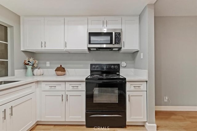 kitchen featuring black electric range oven, light hardwood / wood-style flooring, and white cabinets