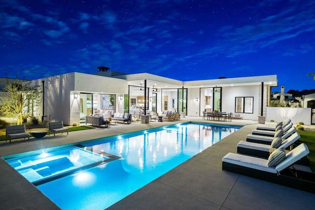 pool at night with an outdoor living space, a patio area, and an in ground hot tub