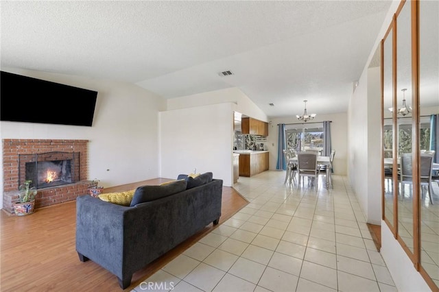 living room featuring lofted ceiling, light tile patterned floors, a brick fireplace, and an inviting chandelier