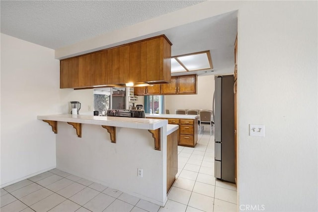 kitchen with a kitchen bar, kitchen peninsula, light tile patterned flooring, stainless steel refrigerator, and a textured ceiling