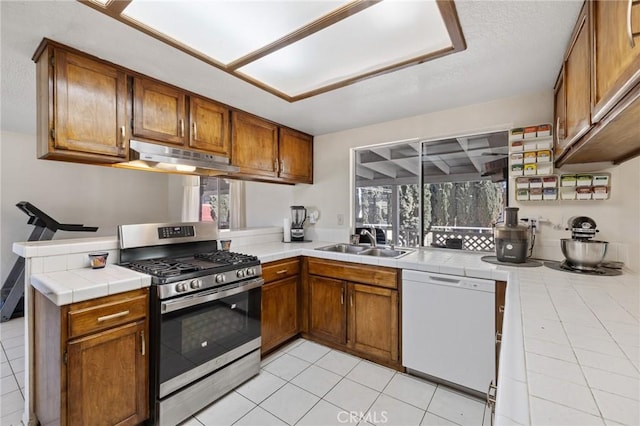 kitchen with tile countertops, kitchen peninsula, sink, white dishwasher, and stainless steel gas range