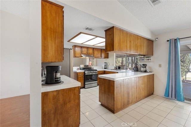 kitchen featuring kitchen peninsula, gas stove, light tile patterned flooring, lofted ceiling, and a textured ceiling