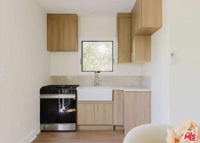 kitchen featuring light wood-type flooring, stainless steel range oven, light brown cabinets, and sink