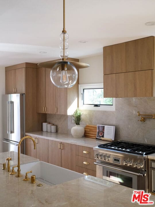 kitchen with premium appliances, decorative backsplash, hanging light fixtures, light stone countertops, and sink