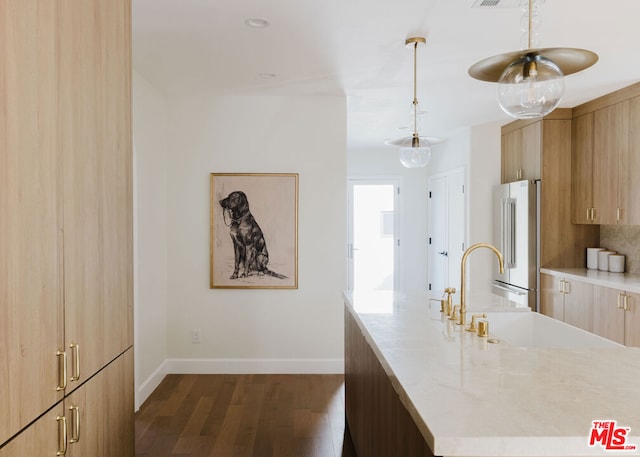 kitchen with decorative backsplash, high end refrigerator, dark hardwood / wood-style flooring, light stone counters, and sink