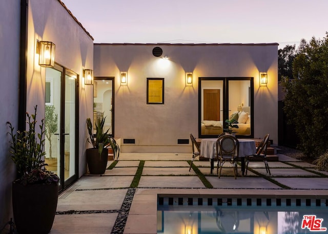 back house at dusk featuring a patio