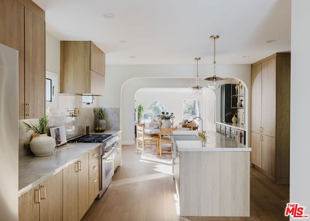 kitchen with high end stainless steel range oven, backsplash, light brown cabinets, and a center island with sink