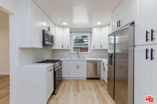 kitchen with light hardwood / wood-style floors, stainless steel appliances, decorative backsplash, white cabinets, and sink