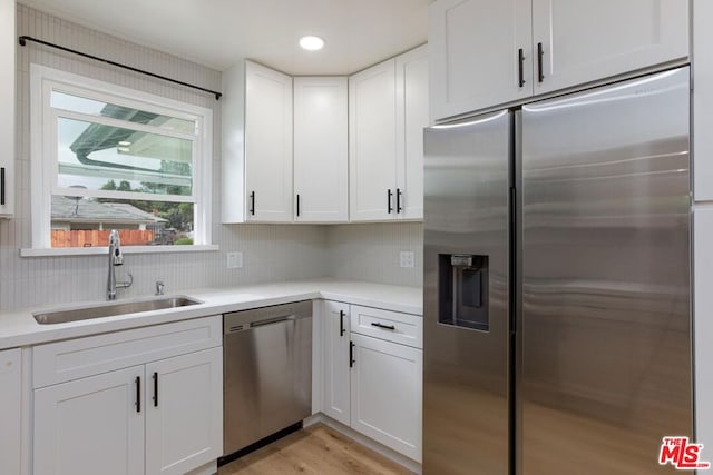 kitchen featuring light hardwood / wood-style floors, stainless steel appliances, backsplash, white cabinets, and sink