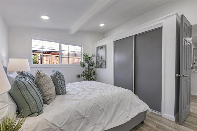 bedroom with wood-type flooring, lofted ceiling with beams, and a closet