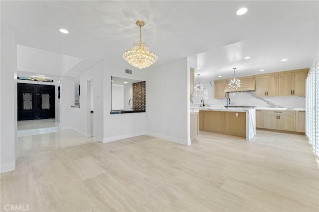 kitchen with tasteful backsplash, a center island, a chandelier, light brown cabinets, and pendant lighting