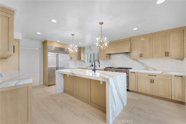 kitchen with custom exhaust hood, decorative light fixtures, a center island with sink, light brown cabinets, and high quality appliances