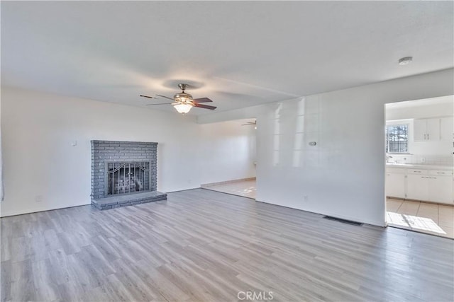 unfurnished living room featuring ceiling fan, light wood-type flooring, and a fireplace