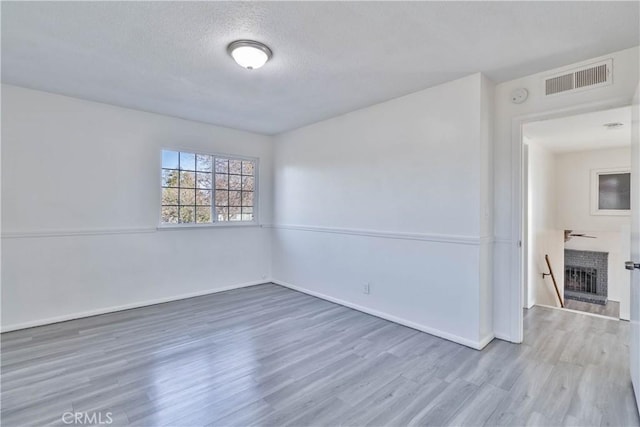 spare room featuring wood-type flooring, a textured ceiling, and a fireplace