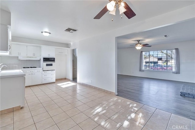 kitchen with backsplash, sink, light tile patterned floors, white oven, and white cabinets