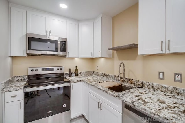 kitchen featuring stainless steel appliances, white cabinetry, light stone counters, and sink