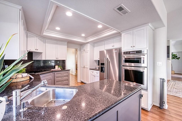 kitchen with white cabinetry, a tray ceiling, stainless steel appliances, and dark stone counters