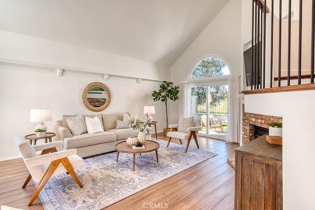 living room featuring high vaulted ceiling, light wood-type flooring, and a fireplace