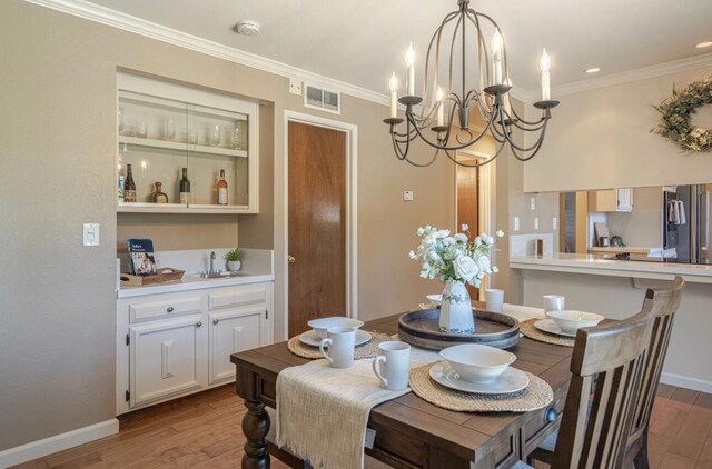 dining area with sink, crown molding, a notable chandelier, and light wood-type flooring