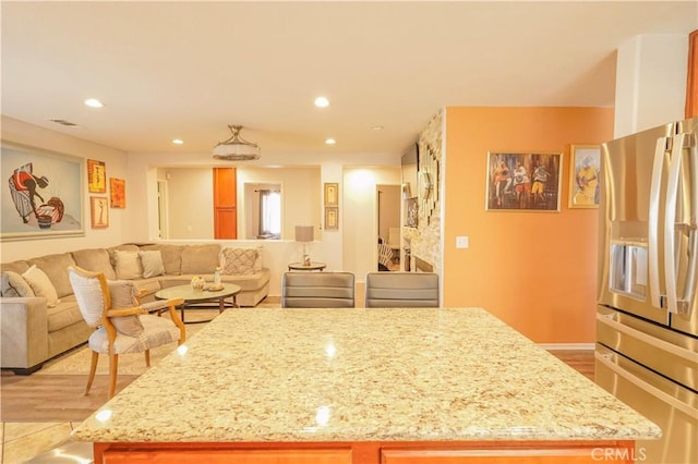 kitchen featuring light stone countertops, stainless steel fridge with ice dispenser, light hardwood / wood-style floors, and a center island