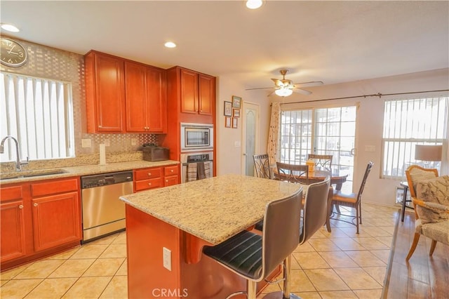 kitchen featuring light tile patterned floors, appliances with stainless steel finishes, light stone countertops, a kitchen island, and sink