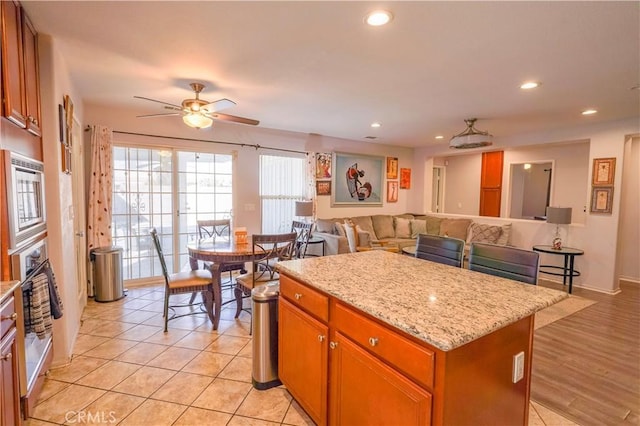 kitchen with a kitchen island, stainless steel appliances, ceiling fan, light stone counters, and light tile patterned floors