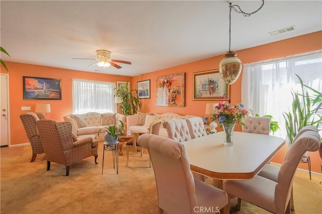 dining space with light carpet, ceiling fan, and plenty of natural light