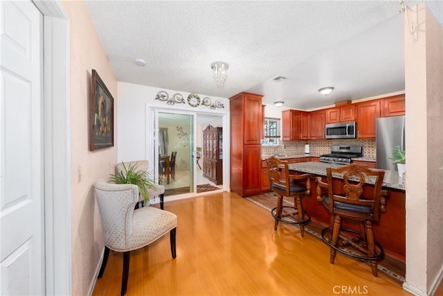 kitchen featuring light wood-type flooring, light stone countertops, decorative backsplash, and stainless steel appliances