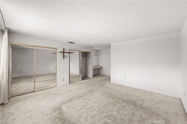 unfurnished bedroom featuring two closets, ensuite bath, light carpet, and a textured ceiling