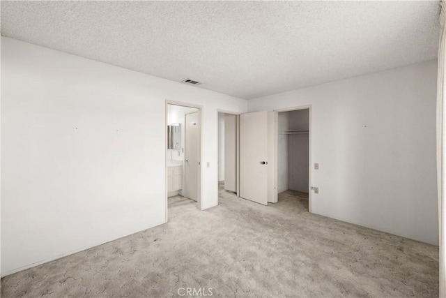 unfurnished bedroom with a closet, a textured ceiling, connected bathroom, and light colored carpet