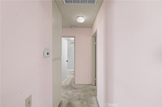 corridor with a textured ceiling and light colored carpet