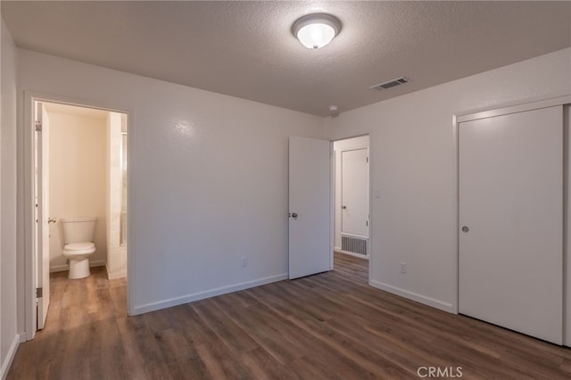 unfurnished bedroom featuring a closet, dark wood-type flooring, connected bathroom, and a textured ceiling