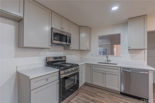 kitchen with light stone counters, sink, stainless steel appliances, and light wood-type flooring