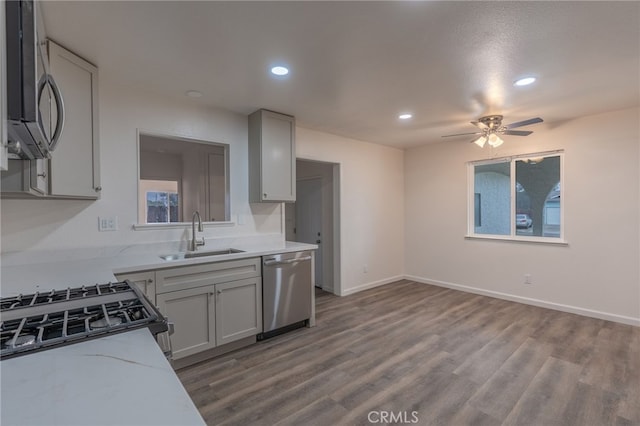 kitchen with ceiling fan, sink, hardwood / wood-style flooring, stainless steel appliances, and light stone counters