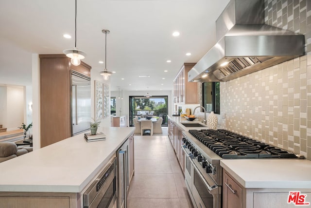 kitchen with decorative light fixtures, wall chimney range hood, built in appliances, tasteful backsplash, and sink