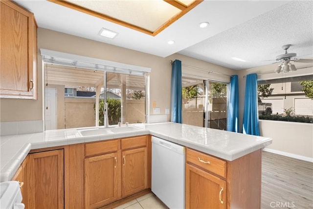 kitchen featuring a textured ceiling, dishwasher, tile counters, sink, and kitchen peninsula