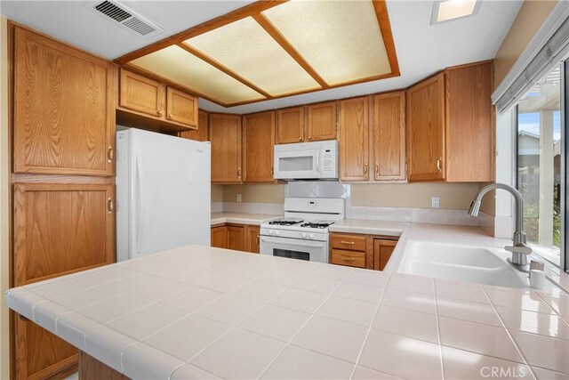 kitchen with white appliances, sink, kitchen peninsula, plenty of natural light, and tile countertops