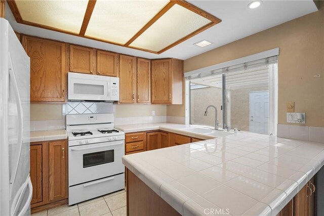 kitchen with kitchen peninsula, sink, light tile patterned flooring, white appliances, and tile countertops