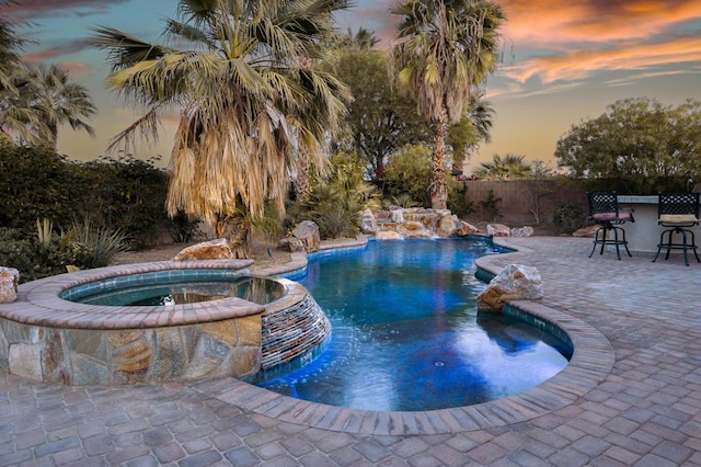 pool at dusk with a bar, an in ground hot tub, and a patio