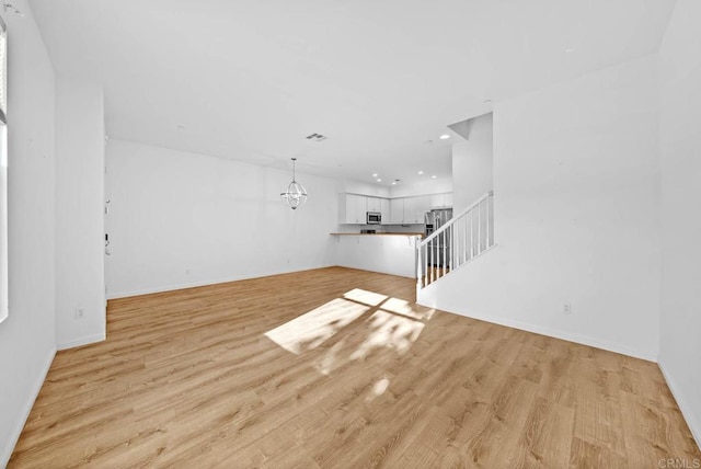 unfurnished living room featuring a notable chandelier and light wood-type flooring