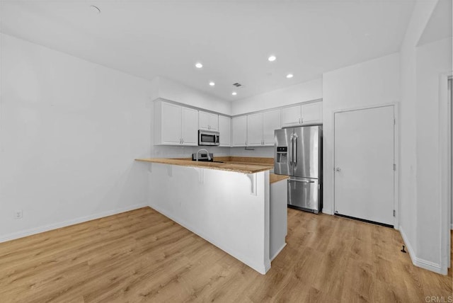 kitchen featuring white cabinetry, kitchen peninsula, a breakfast bar area, appliances with stainless steel finishes, and light wood-type flooring