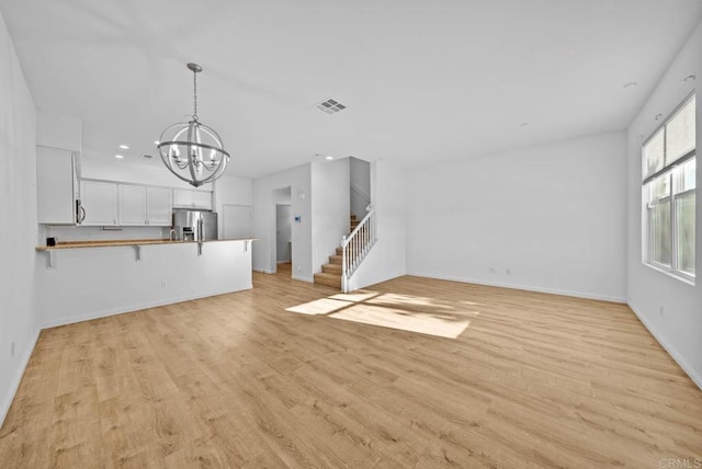 unfurnished living room with light wood-type flooring and a chandelier