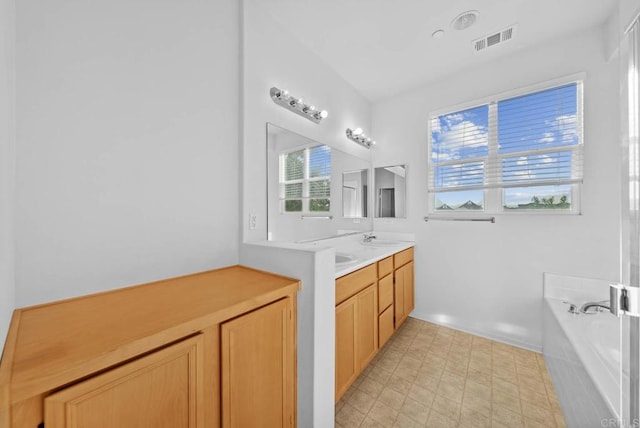 bathroom featuring plenty of natural light, tiled tub, and vanity